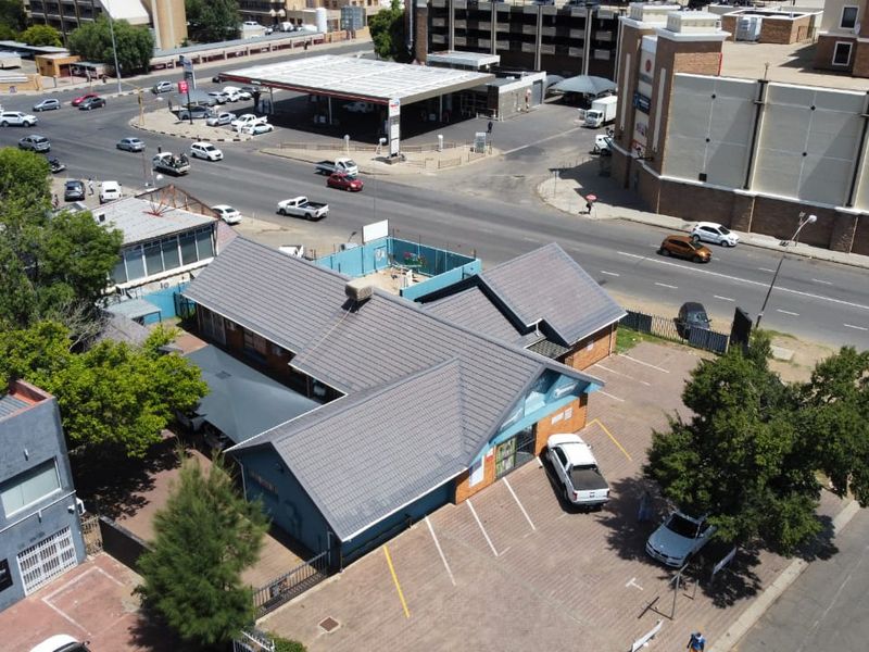 Aerial view of a commercial property featuring a tiled roof building with an adjacent paved parking area, situated in a busy urban street location.