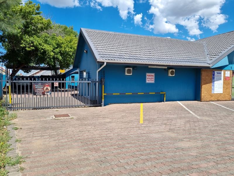 Commercial property exterior featuring a paved parking area, secure metal gate, electric fencing, and blue painted facade with external air conditioning units.