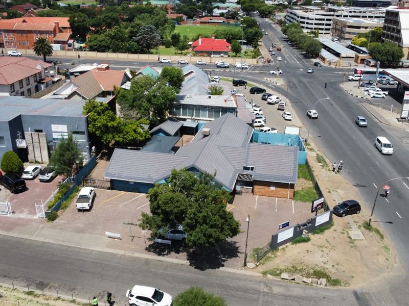 Aerial view of a commercial property featuring a tiled roof building, paved parking area, and direct access to a main road intersection.