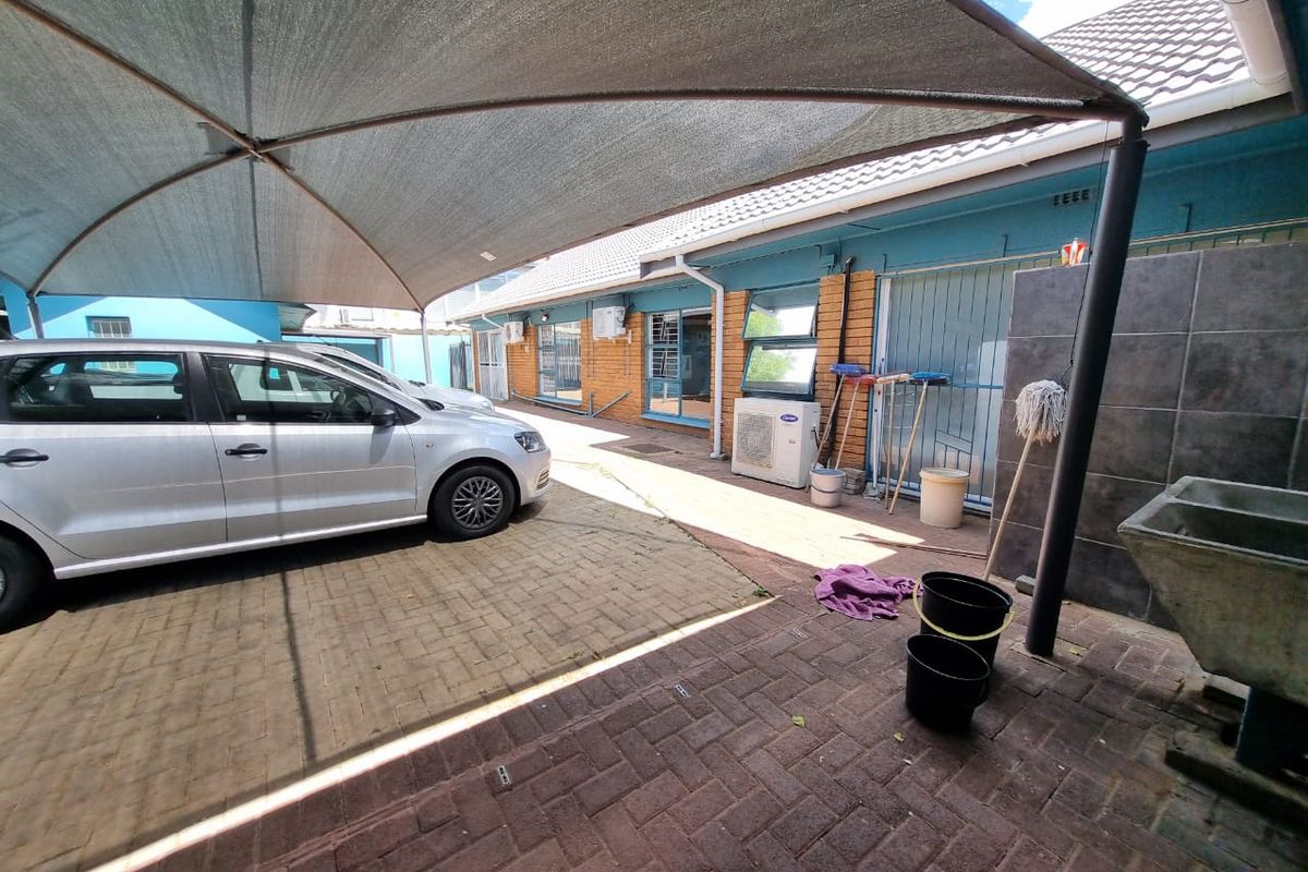 Rear exterior area featuring a paved driveway with a shade sail, security gates, and a utility sink area.