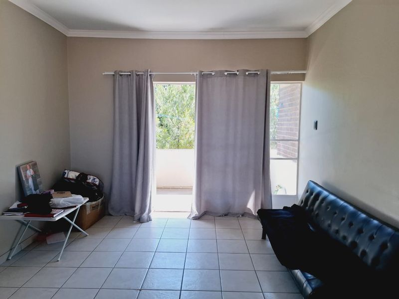 A living room featuring neutral tiled flooring and a sliding glass door providing access to an outdoor balcony area.