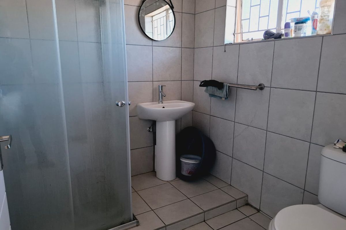 A functional bathroom featuring a pedestal basin, a glass shower enclosure, and a toilet, finished with neutral wall and floor tiles.