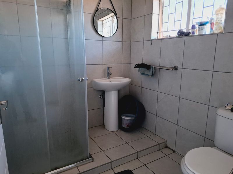 A functional bathroom featuring a pedestal basin, a glass shower enclosure, and a toilet, finished with neutral wall and floor tiles.