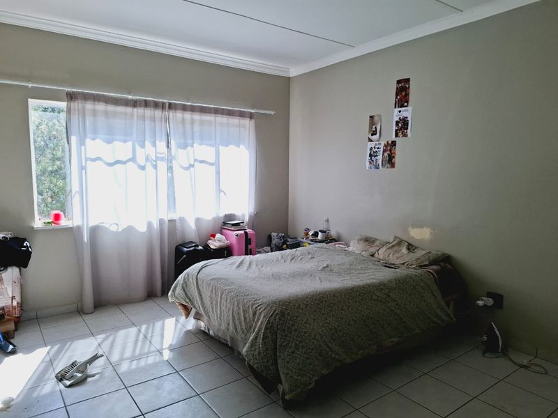 A bedroom featuring tiled flooring and cornicing, with visible wall surface damage near the bed area.