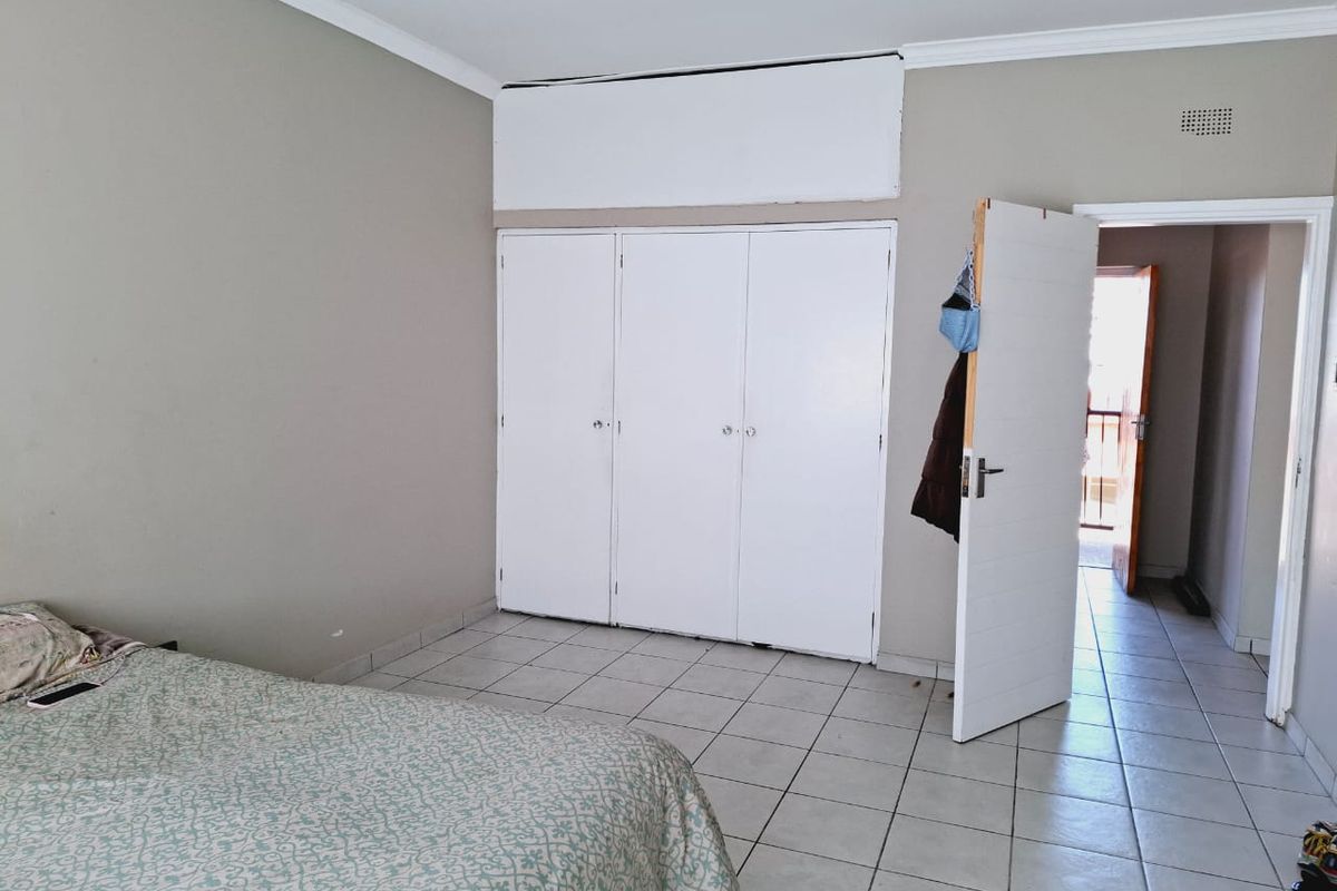 A bedroom featuring tiled flooring and built-in cupboards, with an open doorway leading to an adjacent space.