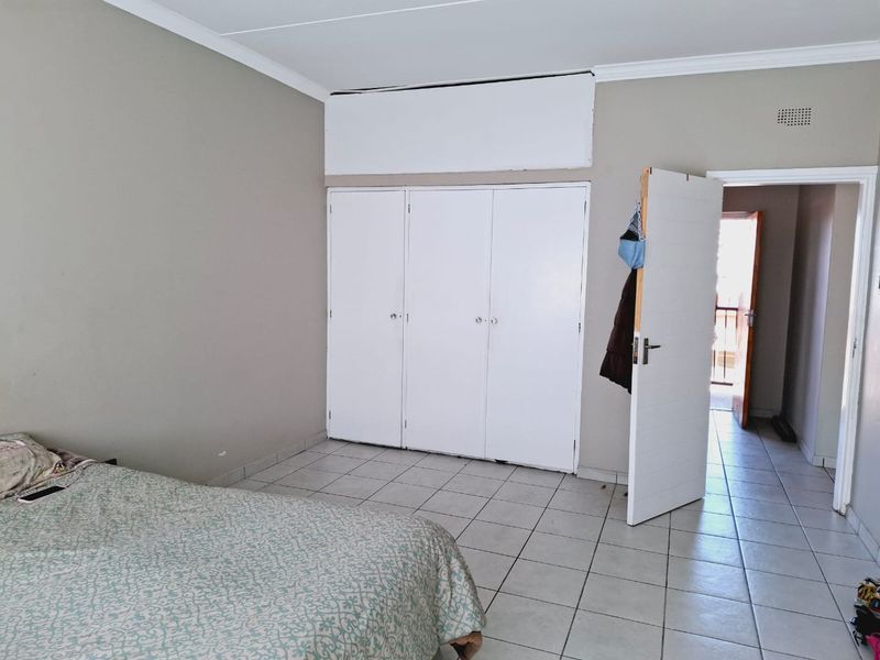A bedroom featuring tiled flooring and built-in cupboards, with an open doorway leading to an adjacent space.