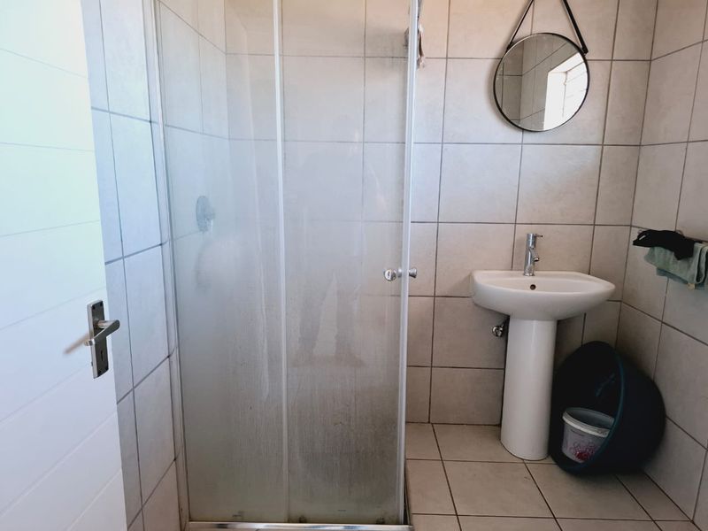 A functional bathroom featuring a pedestal basin, mixer tap, and a glass-enclosed shower with neutral ceramic wall and floor tiling.