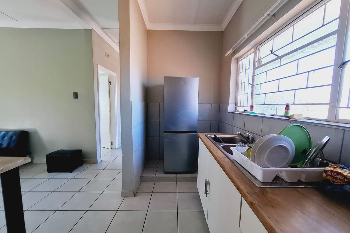 A functional kitchen area featuring white cabinetry, a wooden countertop, stainless steel sink, and tiled flooring, with natural light from a window with security bars.