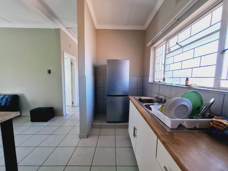 A functional kitchen area featuring white cabinetry, a wooden countertop, stainless steel sink, and tiled flooring, with natural light from a window with security bars.