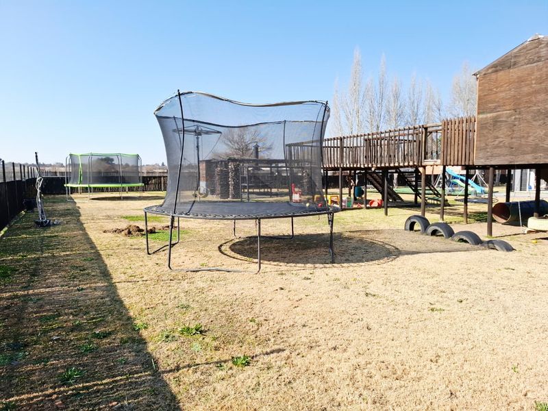 Spacious backyard garden featuring a large wooden play structure and open lawn area, suitable for outdoor recreation.