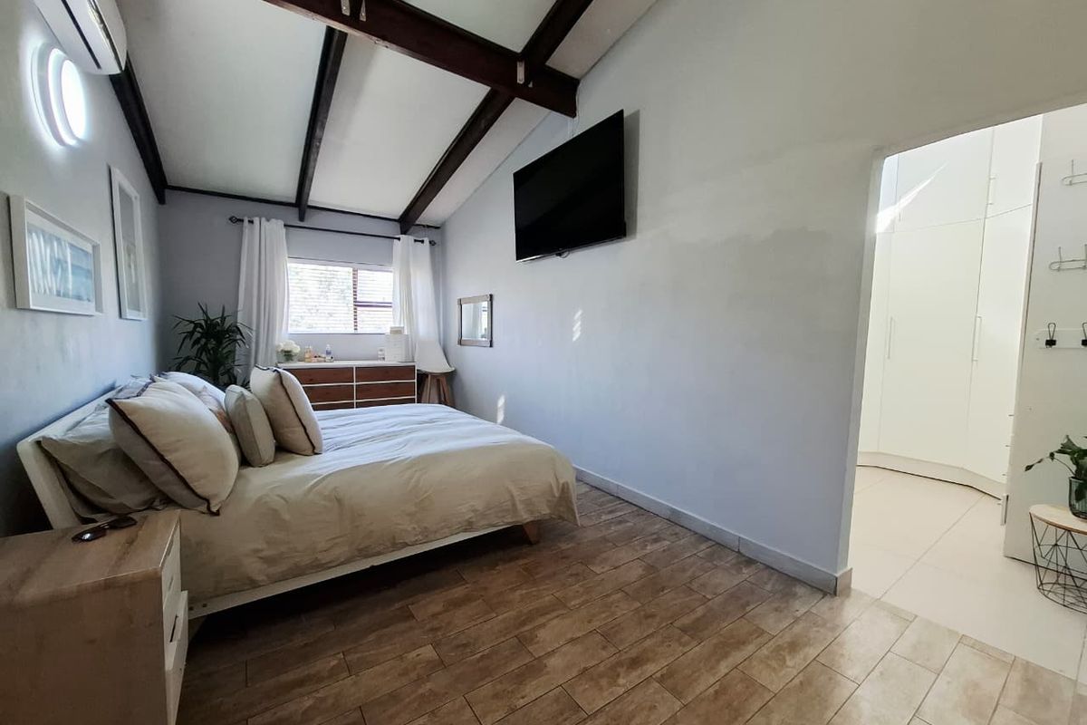 Spacious bedroom featuring exposed timber ceiling beams, tiled flooring, and an adjoining walk-in closet area with built-in cabinetry.