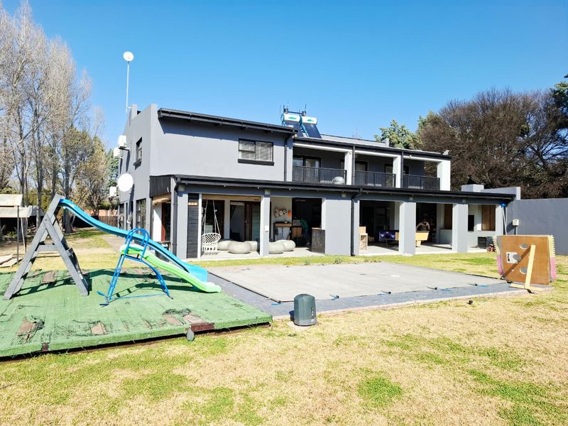 Rear view of a two-story house featuring a covered patio, upper balcony, solar water heating, and a swimming pool with a safety cover.