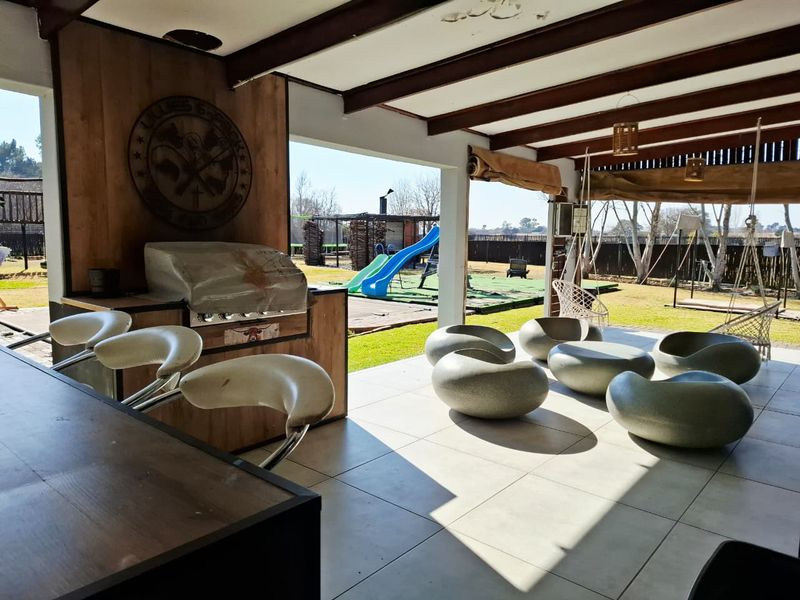 Spacious covered patio featuring tiled flooring, exposed timber beams, and a built-in braai area, overlooking the garden and play area.