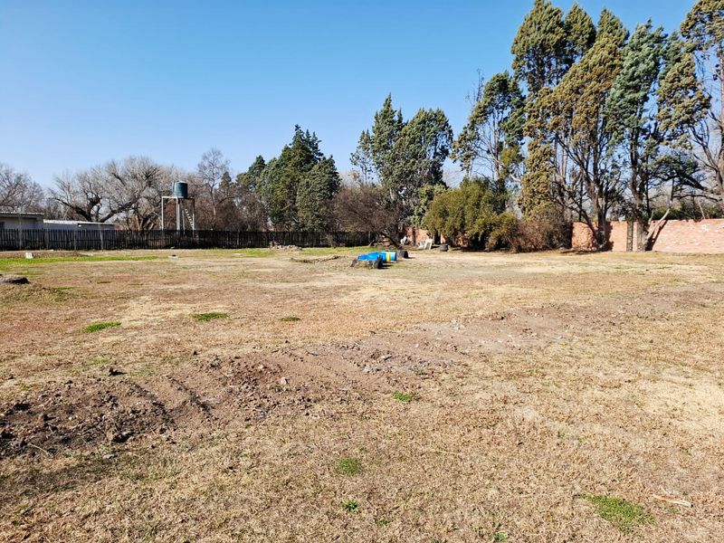 A large, open, undeveloped garden area featuring a water tank, perimeter fencing, and a brick boundary wall.