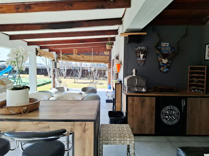 A spacious covered patio featuring exposed timber beams, built-in bar cabinetry, and direct access to the rear garden area.