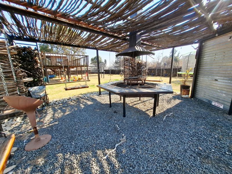 Outdoor entertainment area featuring a rustic timber pergola, central built-in braai, and gravel flooring, ideal for social gatherings.