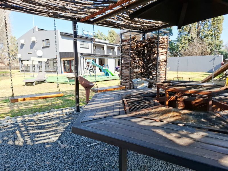 Outdoor entertainment area featuring a built-in braai, pergola structure, and wood storage, overlooking a spacious garden with a play area.