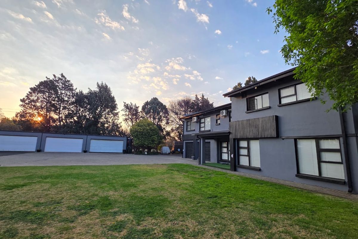 Spacious rear exterior view featuring a large lawn, paved driveway, and a triple garage attached to a modern two-story residential building.