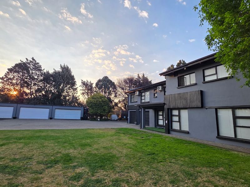 Spacious rear exterior view featuring a large lawn, paved driveway, and a triple garage attached to a modern two-story residential building.