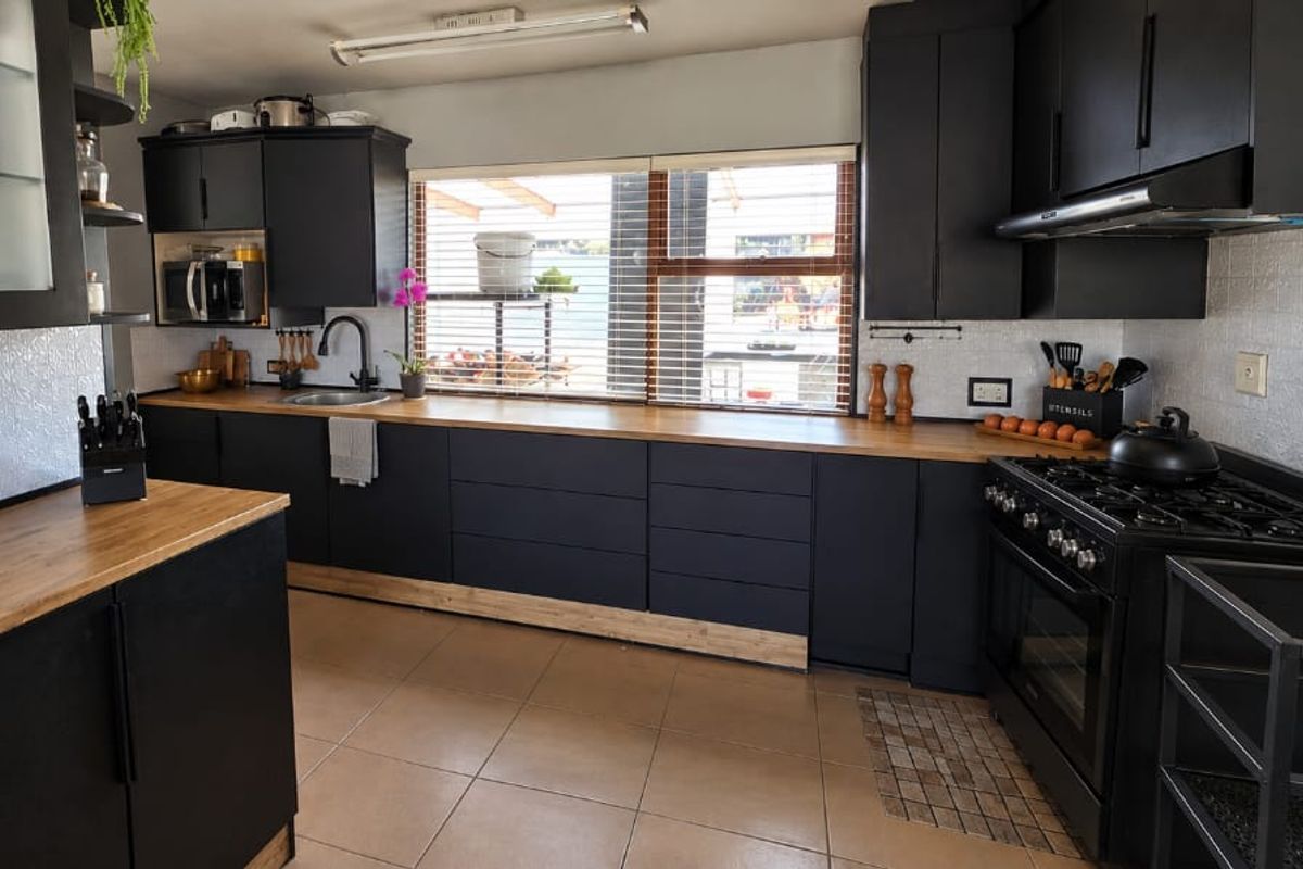 Modern kitchen featuring matte black cabinetry, warm wooden countertops, a gas stove with extractor fan, and a textured backsplash.