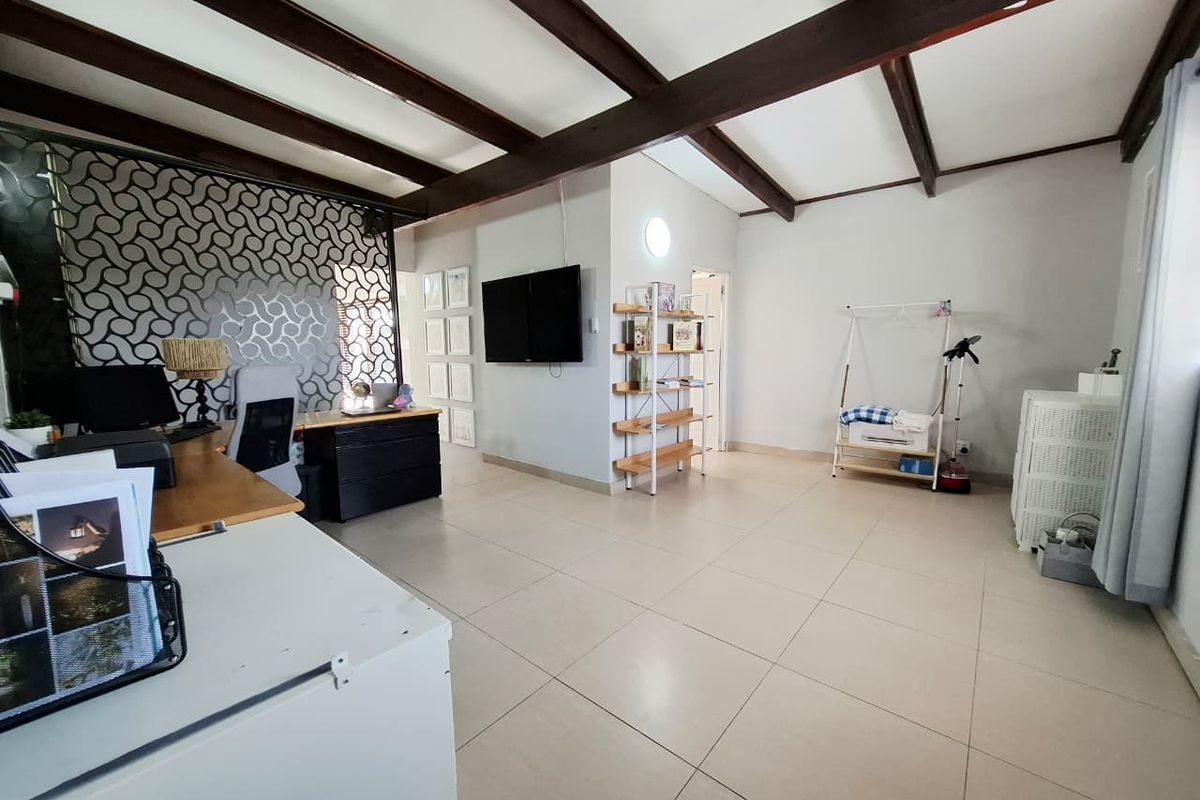 Spacious living area featuring exposed timber ceiling beams, neutral tiled flooring, and a decorative room divider, offering a versatile layout for various uses.