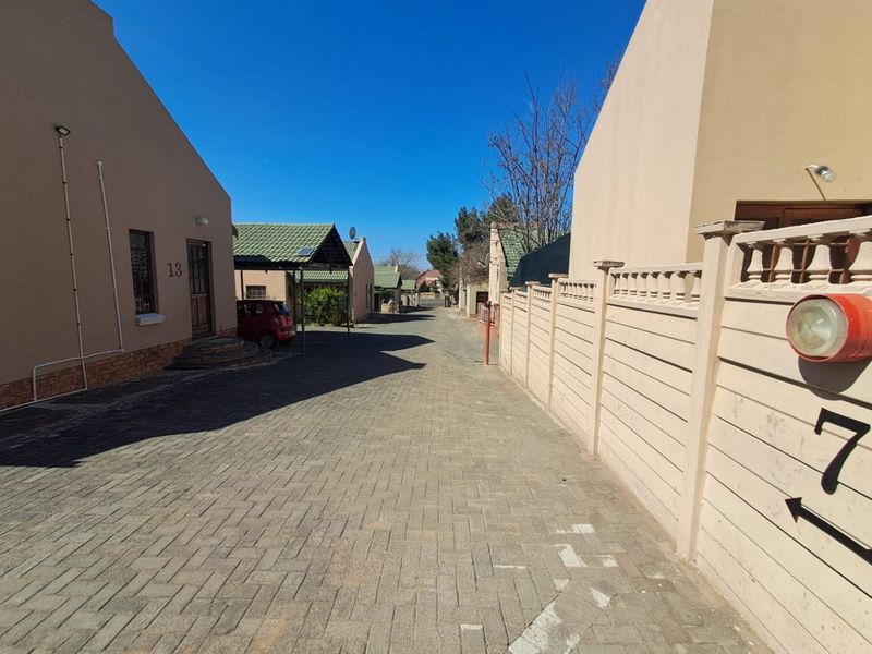 A view of the paved driveway and access road within the townhouse complex, showing the exterior facades and boundary walls of the units.