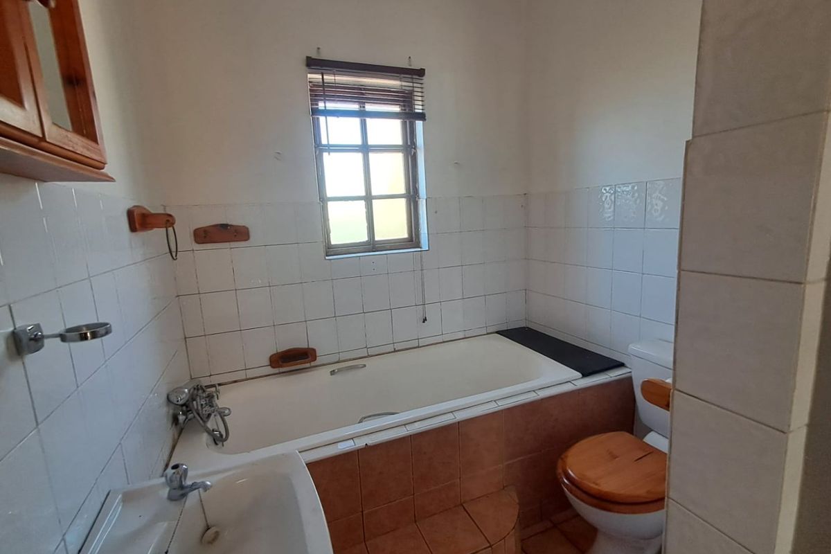 A dated bathroom featuring a built-in bathtub, toilet, and washbasin with tiled finishes, offering potential for modernization and renovation.