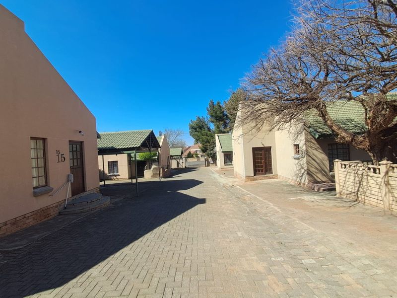 A view of the townhouse complex driveway featuring paved surfaces, multiple residential units with tiled roofs, and established trees.
