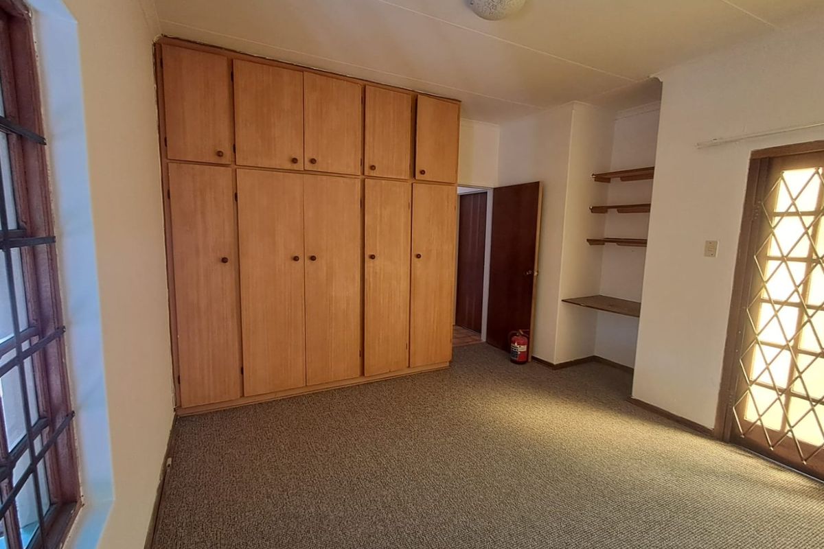 A spacious bedroom featuring extensive built-in wooden cabinetry, integrated shelving, carpeted flooring, and direct access to an exterior door with security gate.