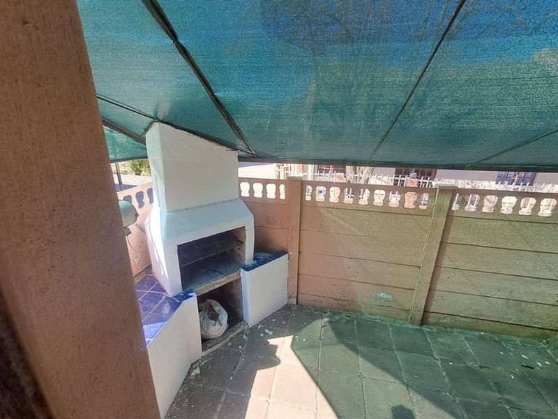 Outdoor patio area featuring a built-in braai, tiled flooring, and a shade cloth canopy, enclosed by a precast concrete boundary wall.