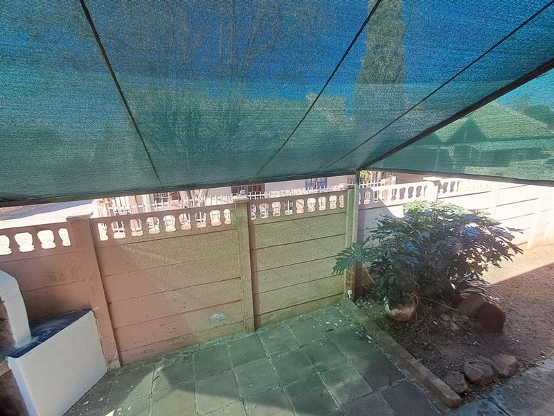 Outdoor patio area featuring a shade cloth canopy, paved flooring, and a built-in braai, enclosed by a precast concrete boundary wall.