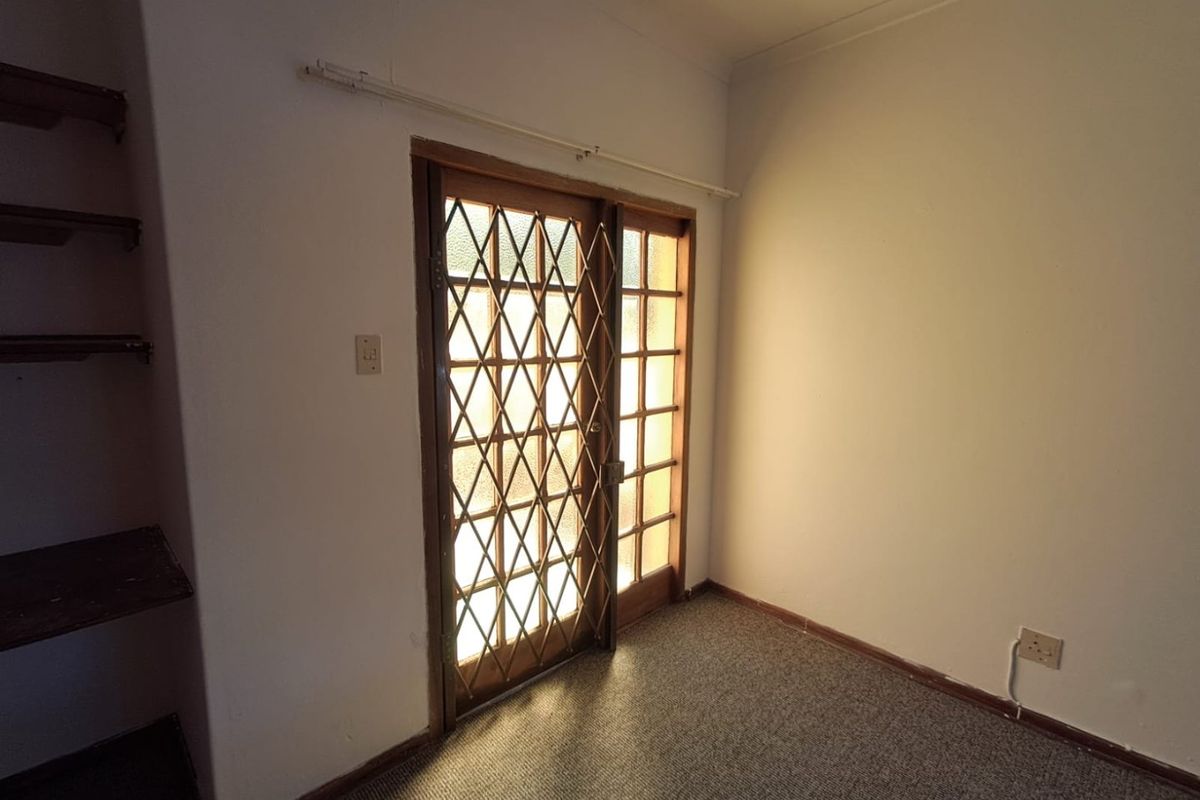 An empty living area featuring built-in shelving, carpet flooring, and a timber-framed glass door with a security gate.