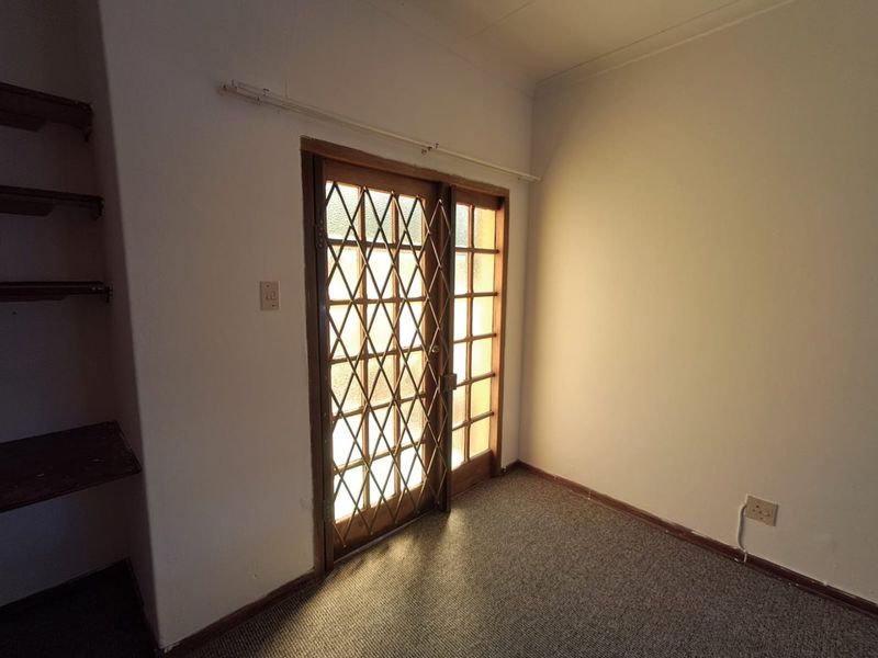 An empty living area featuring built-in shelving, carpet flooring, and a timber-framed glass door with a security gate.
