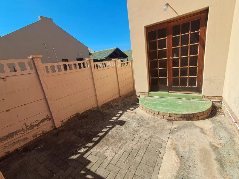 Rear courtyard area featuring paved flooring, a raised brick step, and timber-framed French doors leading into the home, enclosed by a precast boundary wall.