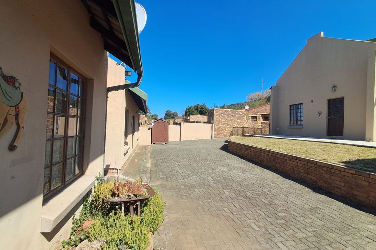 A view of the rear exterior area featuring a paved driveway, brick retaining wall, and a small lawn section.
