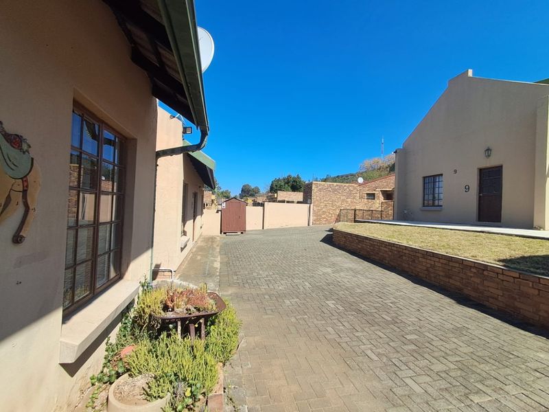 A view of the rear exterior area featuring a paved driveway, brick retaining wall, and a small lawn section.