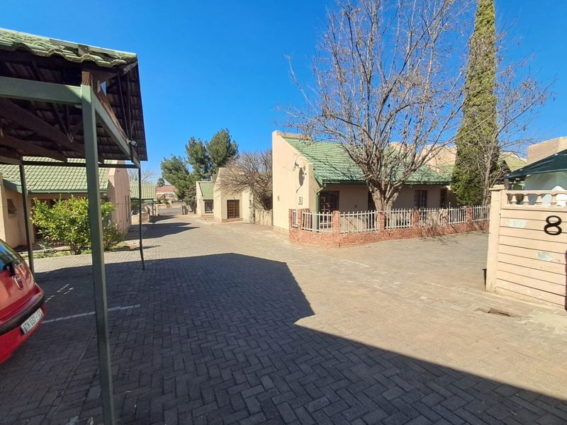 View of the townhouse complex driveway featuring paved surfaces, brick boundary walls, and established residential units with tiled roofs.