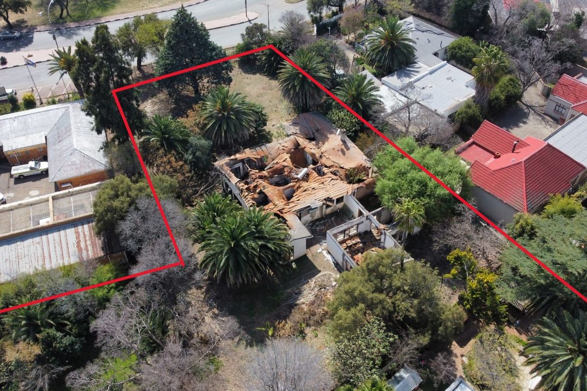 Aerial view of a property featuring a large garden with mature trees and a building showing severe structural damage and a collapsed roof.