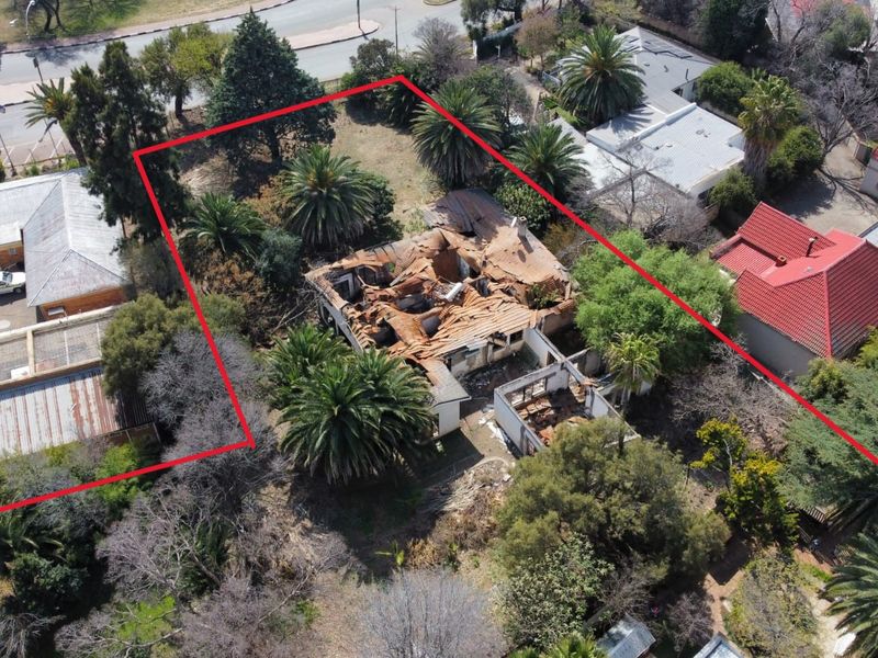 Aerial view of a property featuring a large garden with mature trees and a building showing severe structural damage and a collapsed roof.