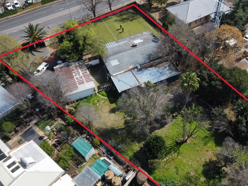 Aerial view of a property featuring a large garden, detached garage, and main dwelling with a corrugated metal roof requiring maintenance.