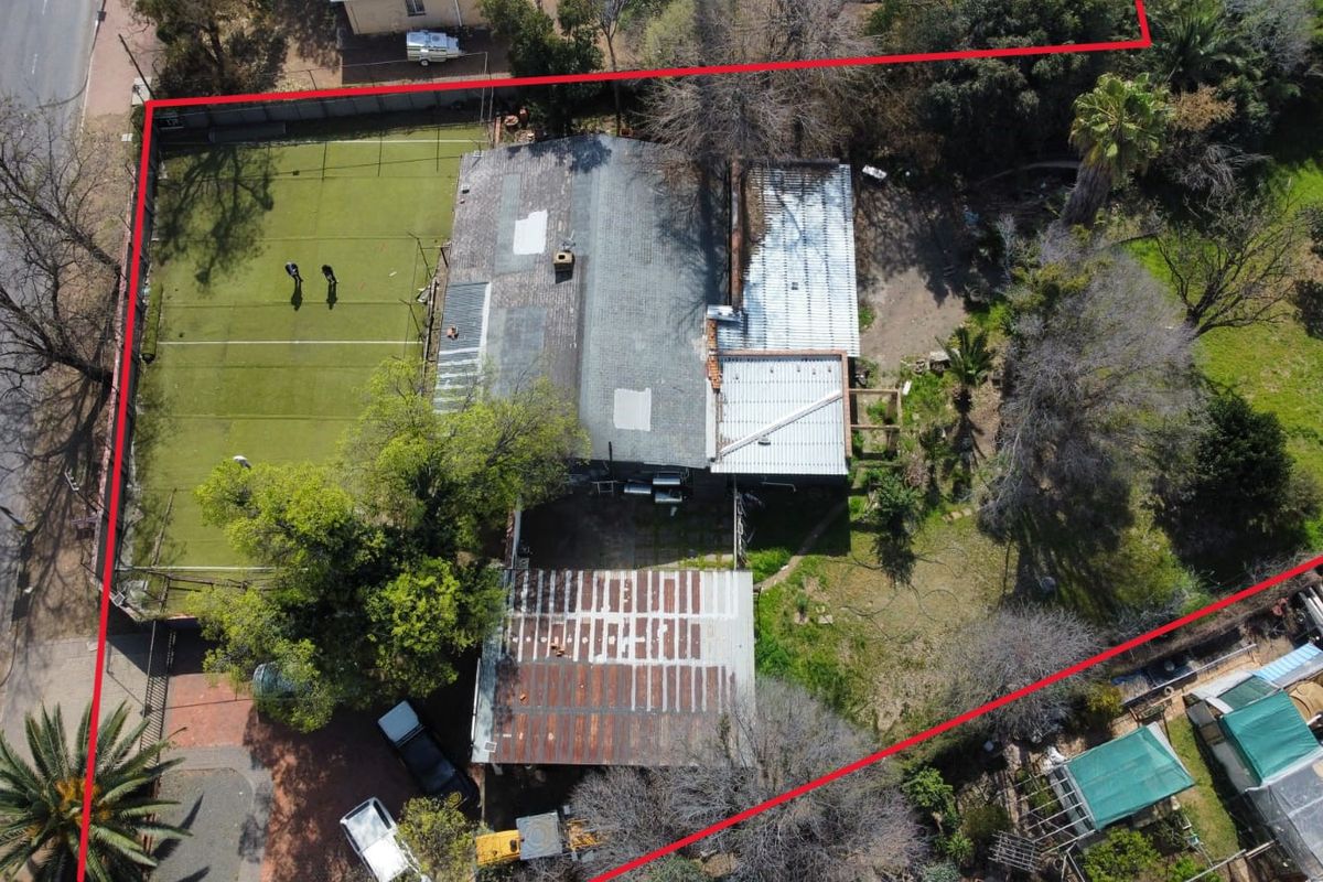Aerial view of the property showing the main dwelling, a tennis court, and surrounding grounds with visible roof maintenance requirements.