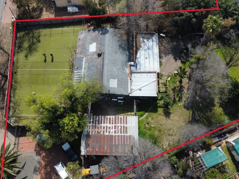 Aerial view of the property showing the main dwelling, a tennis court, and surrounding grounds with visible roof maintenance requirements.