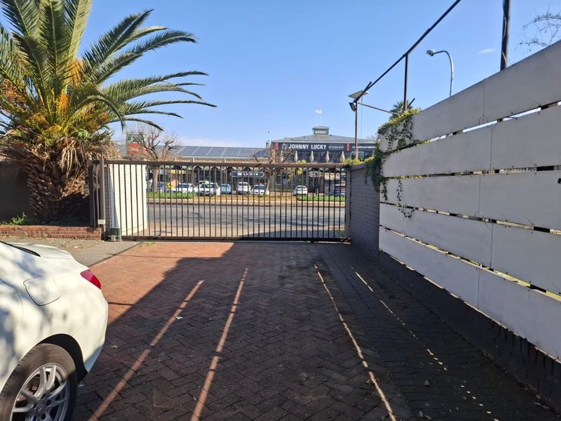 Front entrance area featuring a metal sliding gate, brick paved driveway, and a white timber slat boundary fence.