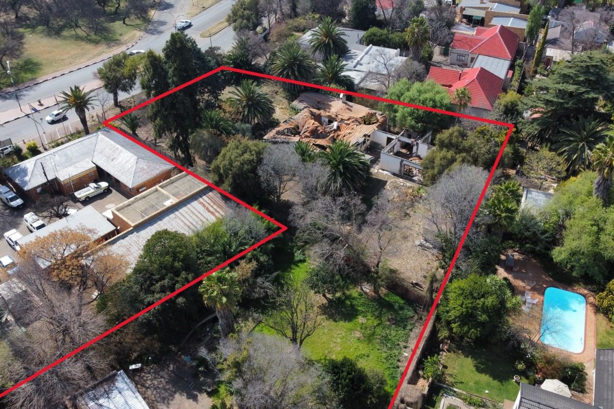 Aerial view of a property featuring a large plot with mature trees, a swimming pool, and a structure showing significant fire and roof damage.