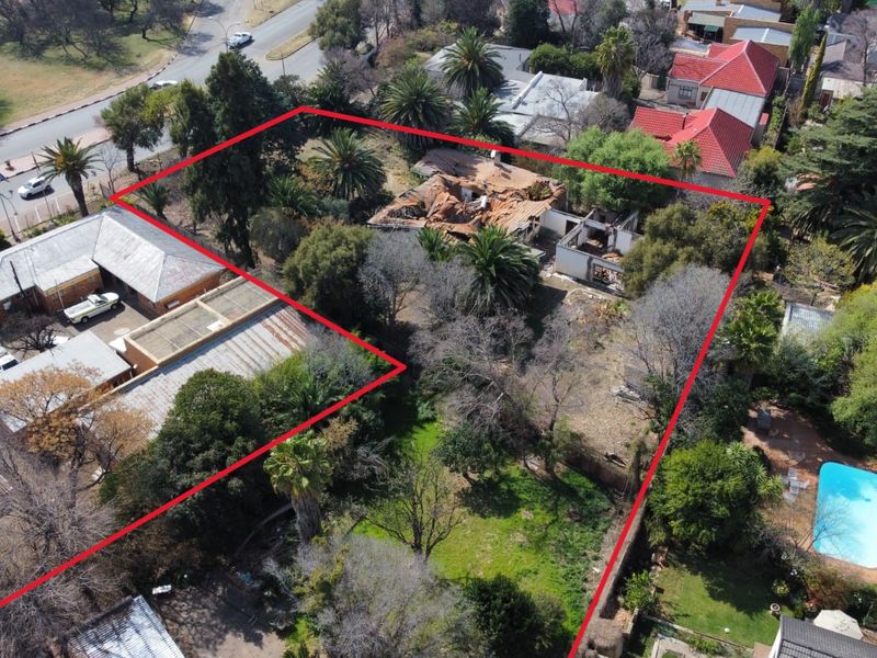 Aerial view of a property featuring a large plot with mature trees, a swimming pool, and a structure showing significant fire and roof damage.