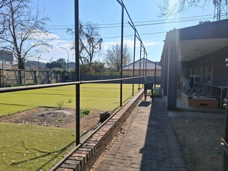Outdoor sports facility featuring artificial turf, perimeter fencing, and a paved walkway adjacent to a covered patio area.