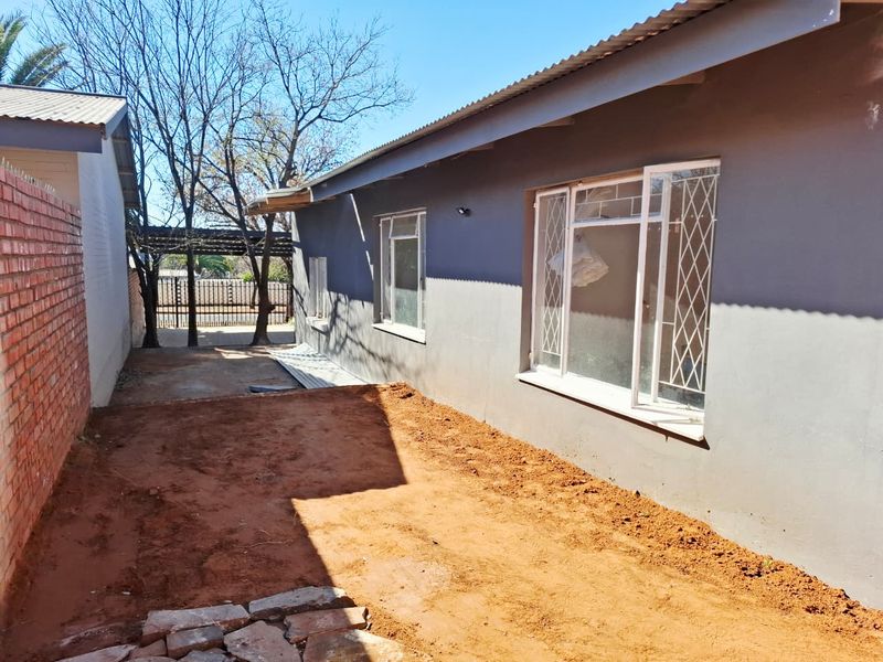 Rear exterior view of the house featuring a grey painted facade, metal security window bars, and an unfinished garden area with exposed soil.