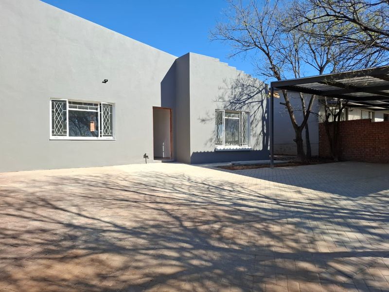 Front exterior view of the property featuring a paved driveway, carport, and grey rendered facade with security-fitted windows.