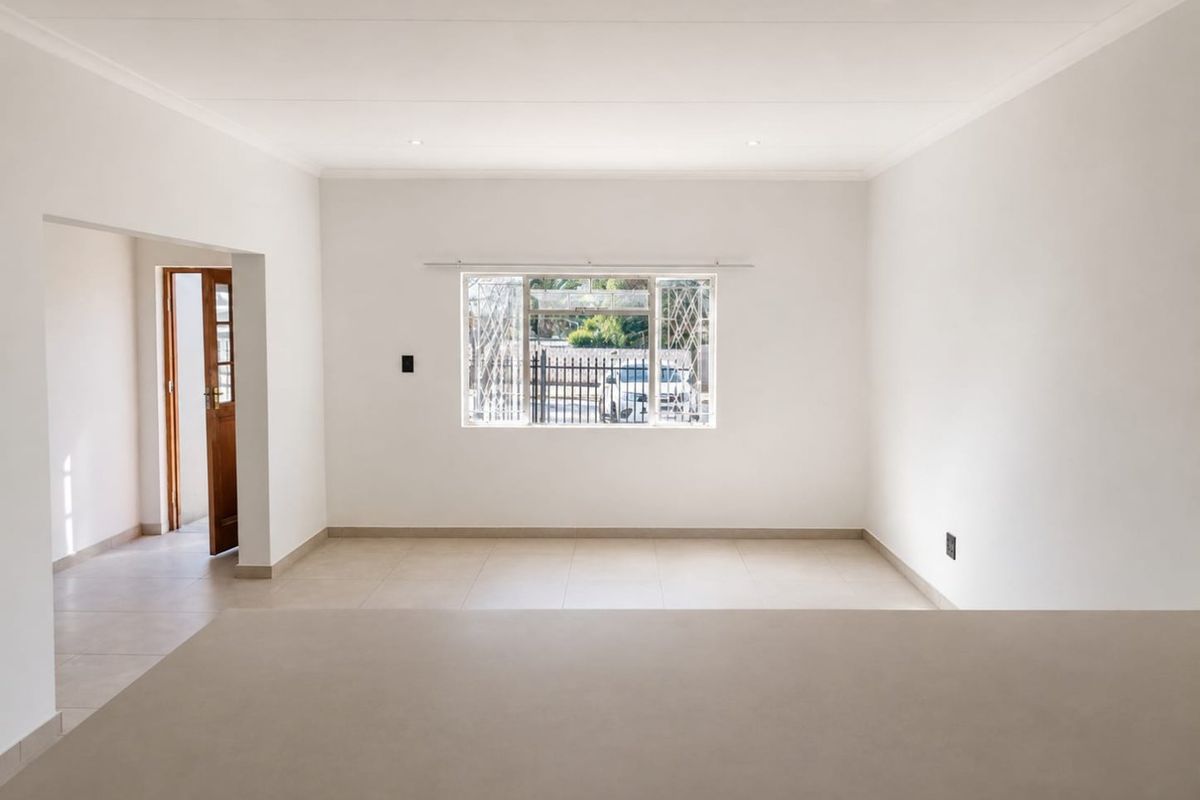 A bright, vacant living area featuring neutral tiled flooring, recessed downlighting, and a secure window overlooking the front exterior.