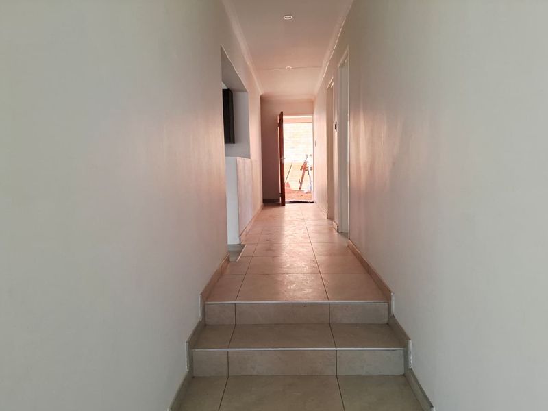 A clean, empty hallway featuring tiled flooring and internal steps leading towards an exterior doorway.